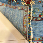 Close-up of turquoise Afghan wool carpet showing its hand-knotted texture, floral border and multicoloured fringe