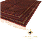 Corner detail of a hand-knotted Afghan wool rug in deep red with repeating diamond medallion motifs and cream fringe — Golden Loom Afghanistan