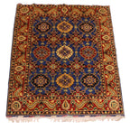 Hand-knotted Afghan wool rug featuring geometric medallions on indigo blue ground with deep red floral border and ivory fringe