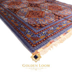 Close-up angled view of Afghan Mamluk carpet pile showing deep blue and burgundy geometric border pattern — Golden Loom Afghanistan
